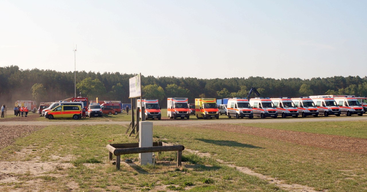 Einsatzkräfte der Feuerwehr und Krankenwagen stehen am Rande eines Waldgebietes.