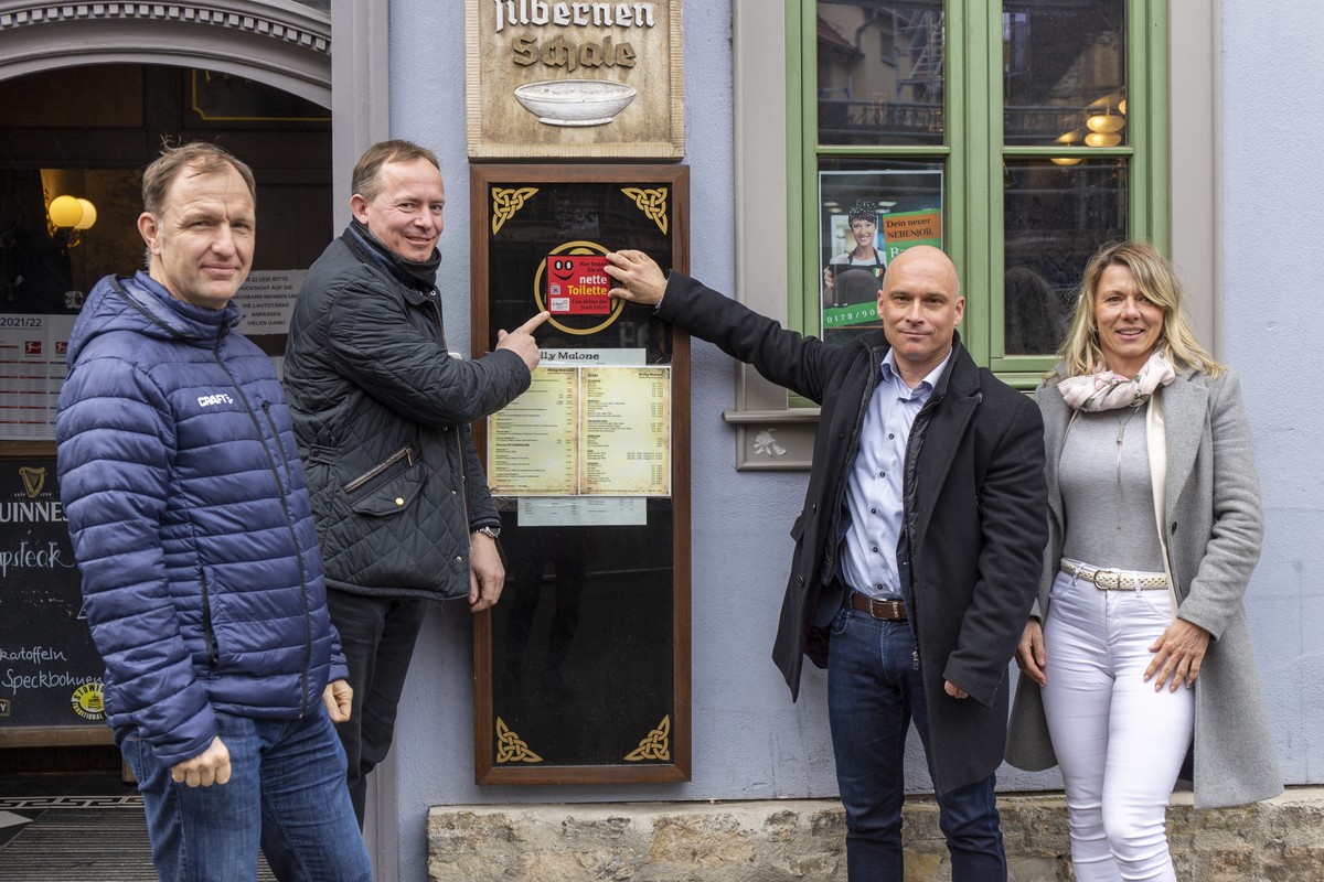 Von links nach rechts: Steffen Linnert (Beigeordneter für Finanzen, Wirtschaft und Digitalisierung), André Grenzdörffer (Gastronom), Andreas Horn (Beigeordneter für Sicherheit und Umwelt) und Patricia Stepputtis (Citymanagerin) bringen in Erfurt einen „nette Toilette“-Aufkleber an.