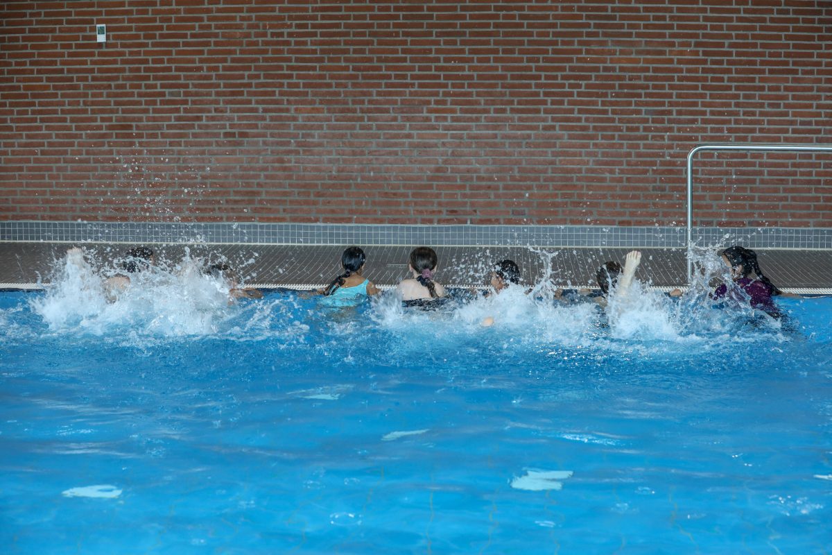 Kinder halten sich am Schwimmbecken fest und machen Ãœbungen