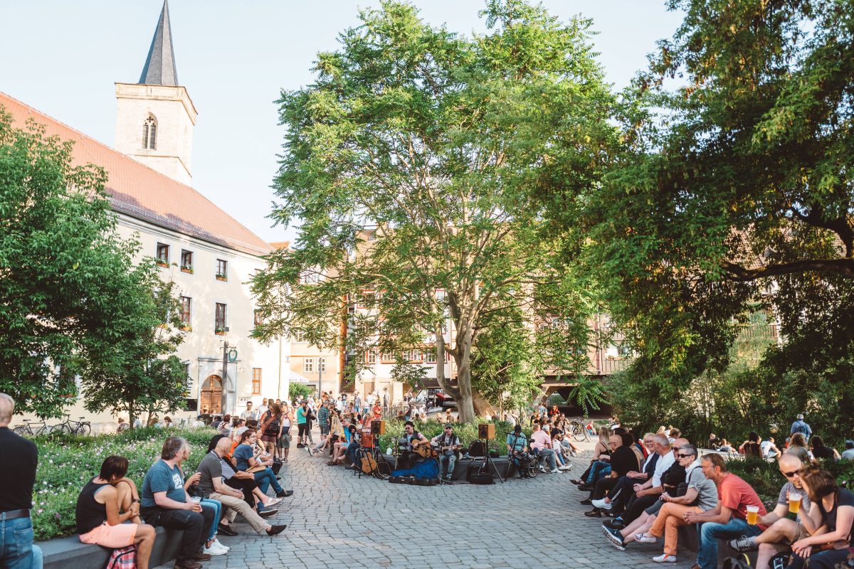 Die Menschen genießen den Sommerabend hinter der Krämerbrücke und lauschen dicht beieinander der Musik.